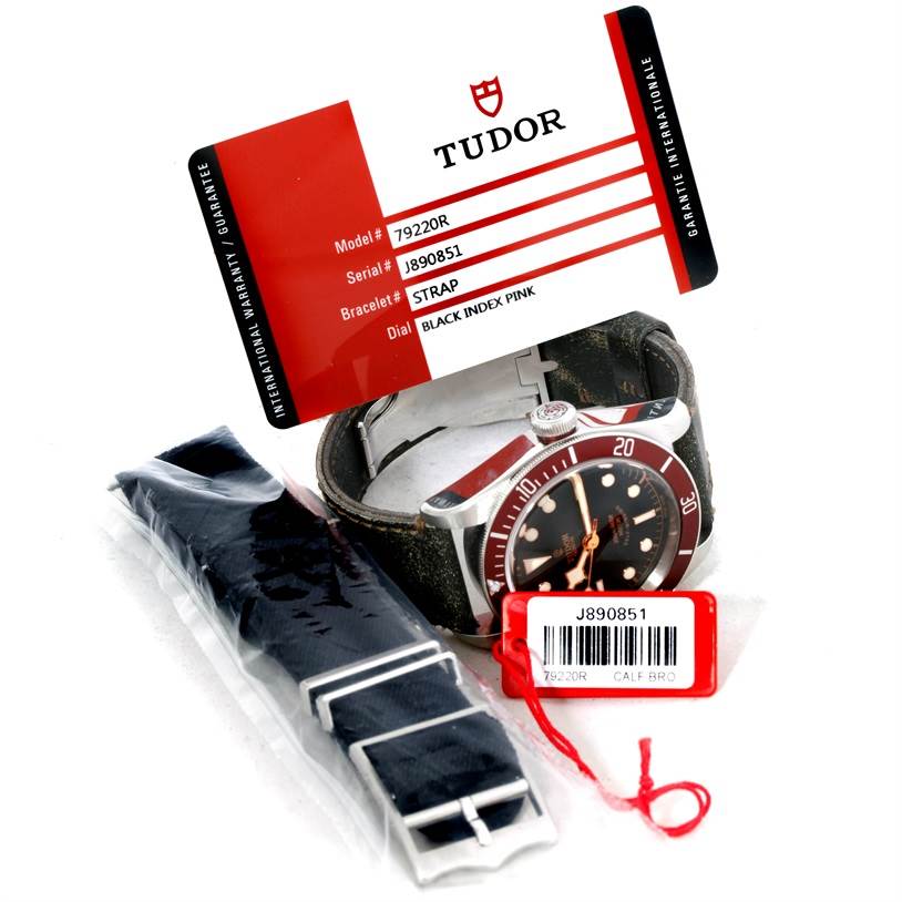 The image shows the Tudor Heritage Black Bay 79220R Men's Stainless Steel Black Dial 79220R Men's Stainless Steel Black Dial watch, its strap, and warranty card from an oblique angle.