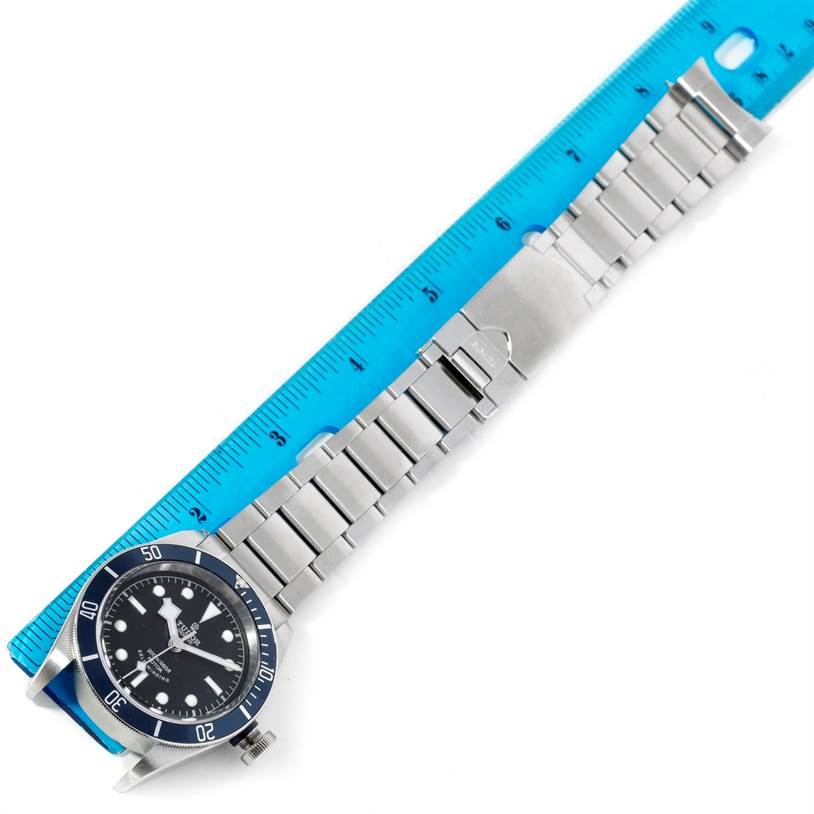 The image shows a Tudor Heritage Black Bay 79220 Men's Stainless Steel Black Dial 79220 Men's Stainless Steel Black Dial watch laid flat next to a blue ruler, highlighting the watch case and bracelet.