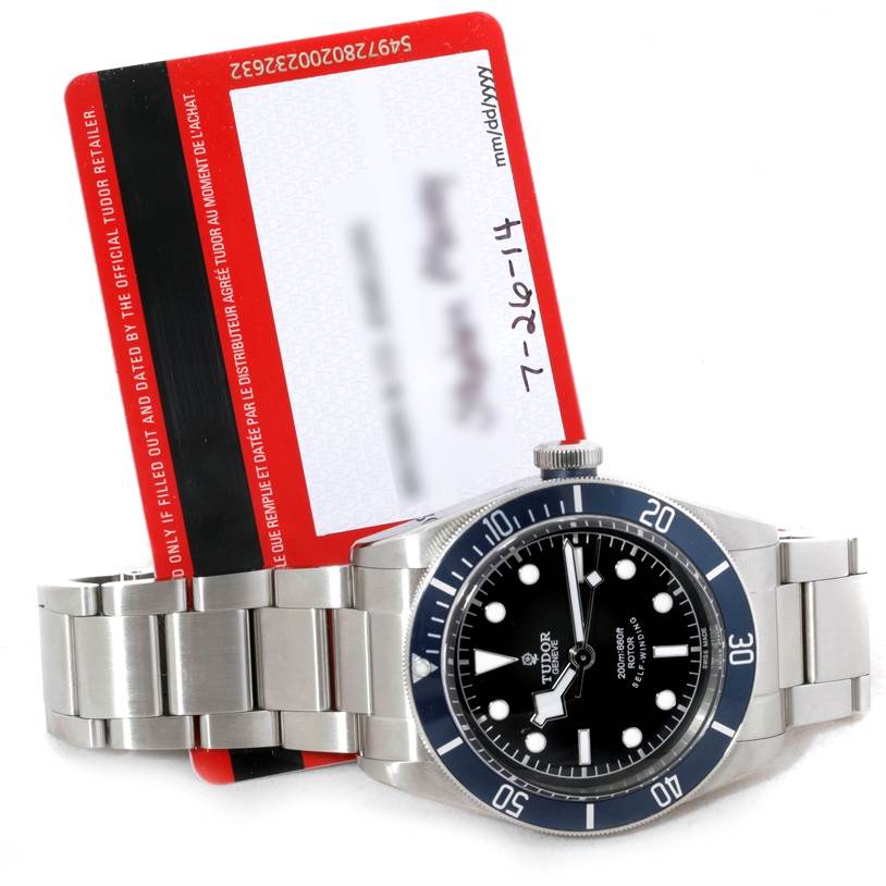 This image shows a Tudor Heritage Black Bay 79220 Men's Stainless Steel Black Dial 79220 Men's Stainless Steel Black Dial watch from a top angle, alongside its warranty card.
