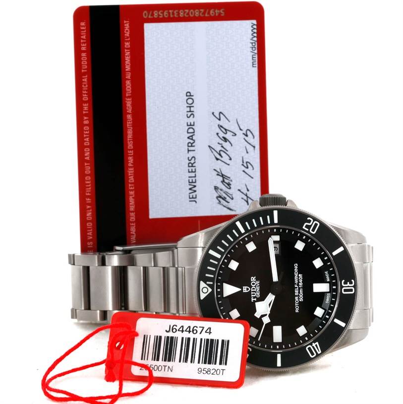 The image shows a Tudor Pelagos 25500TN Men's Titanium Black Dial 25500TN Men's Titanium Black Dial watch viewed from the front, along with its metal bracelet, a warranty card, and a tag.