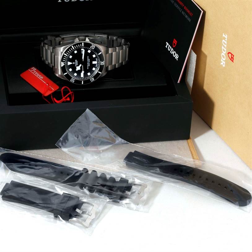 The image shows a Tudor Pelagos 25500TN Men's Titanium Black Dial 25500TN Men's Titanium Black Dial watch with its original bracelet, alongside additional straps still in their packaging.