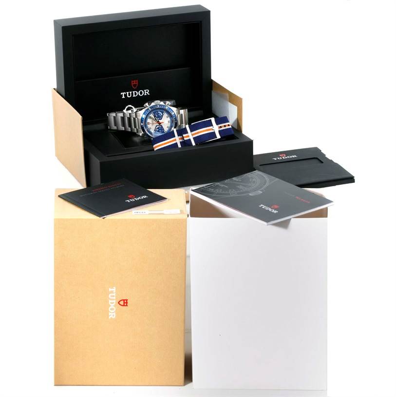The image shows an open Tudor Heritage Chrono 70330 Men's Stainless Steel Blue Dial 70330 Men's Stainless Steel Blue Dial watch box with the watch, additional strap, manuals, and outer packaging.