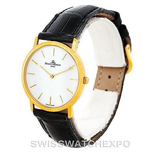 This image shows a Baume & Mercier Classima Men's Yellow Gold White Dial Men's Yellow Gold White Dial watch at a three-quarter angle, highlighting its gold case, white dial, and black leather strap.