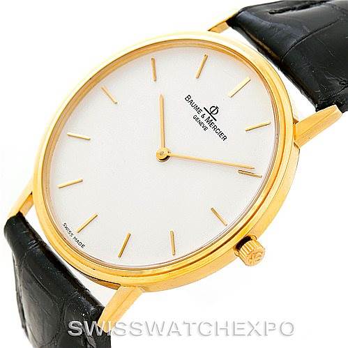 The image shows a three-quarter view of a Baume & Mercier Classima MV045088 Men's Yellow Gold White Dial MV045088 Men's Yellow Gold White Dial watch, highlighting the golden case, white dial, and black leather strap.