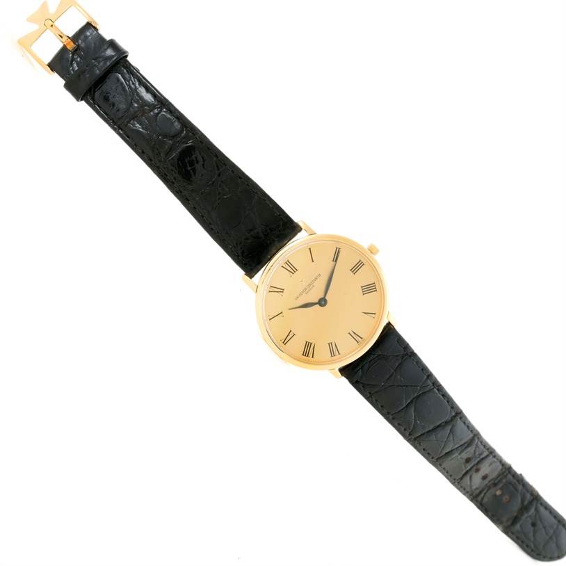 The image shows a Vintage Vacheron Constantin watch with a gold face, black Roman numerals, and a black leather strap from a top-down angle.