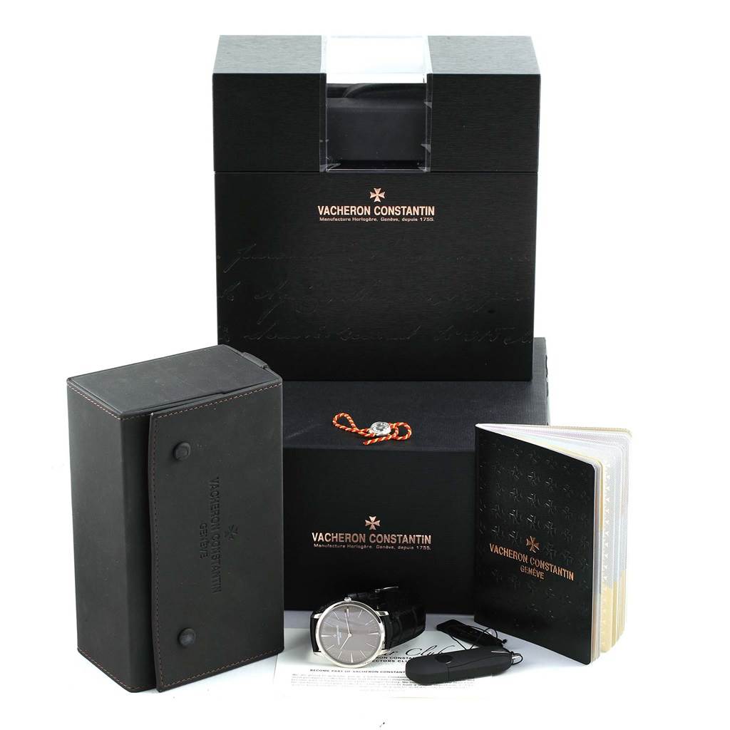 The image shows a Vacheron Constantin Patrimony 81180/000P-9539 Men's Platinum Grey Dial 81180/000P-9539 Men's Platinum Grey Dial watch with its black case, box, manual, and accessories from a front angle.