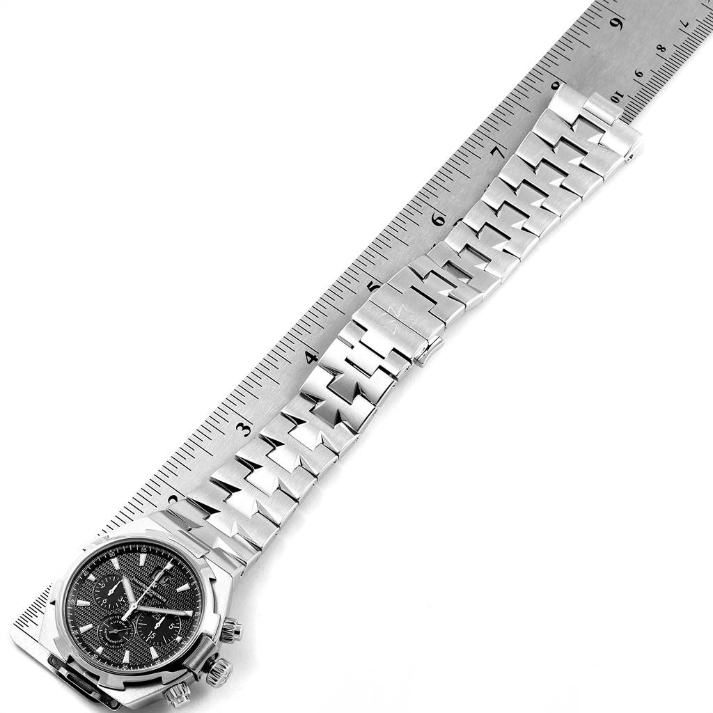 The Vacheron Constantin Overseas 49150.B01A.9097 Men's Stainless Steel Black Dial 49150.B01A.9097 Men's Stainless Steel Black Dial watch is shown from a top angle, featuring the case, dial, buttons, and stainless steel bracelet, measured with a ruler.