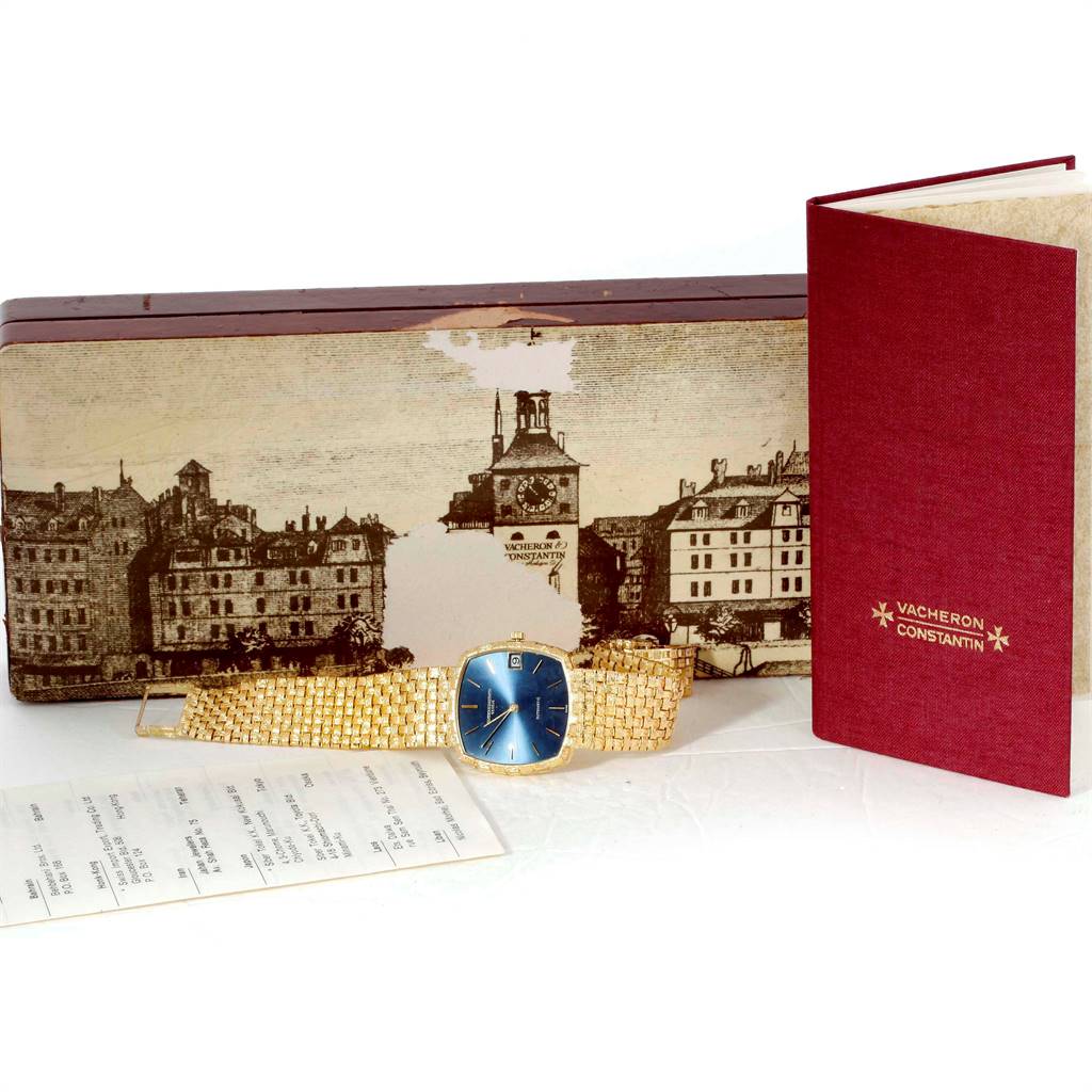 A vintage Vacheron Constantin watch with a blue dial and gold bracelet is displayed with its box and a red booklet.
