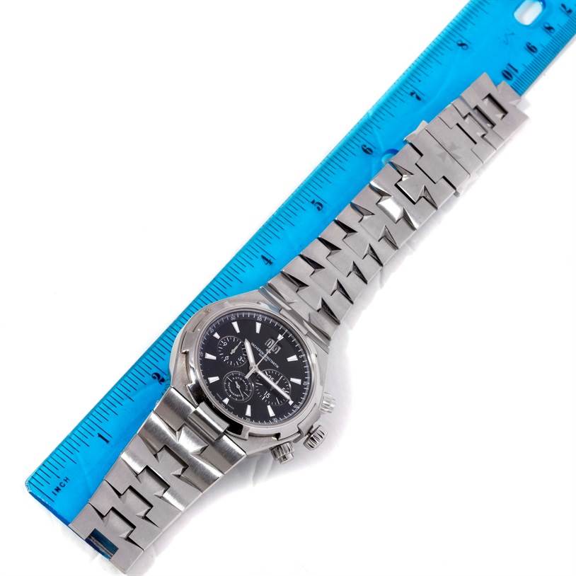 The Vacheron Constantin Overseas 49150.B01A.9097 Men's Stainless Steel Black Dial 49150.B01A.9097 Men's Stainless Steel Black Dial watch is shown from a top-down angle, displaying its face, crown, and stainless steel bracelet positioned next to a blue ruler.