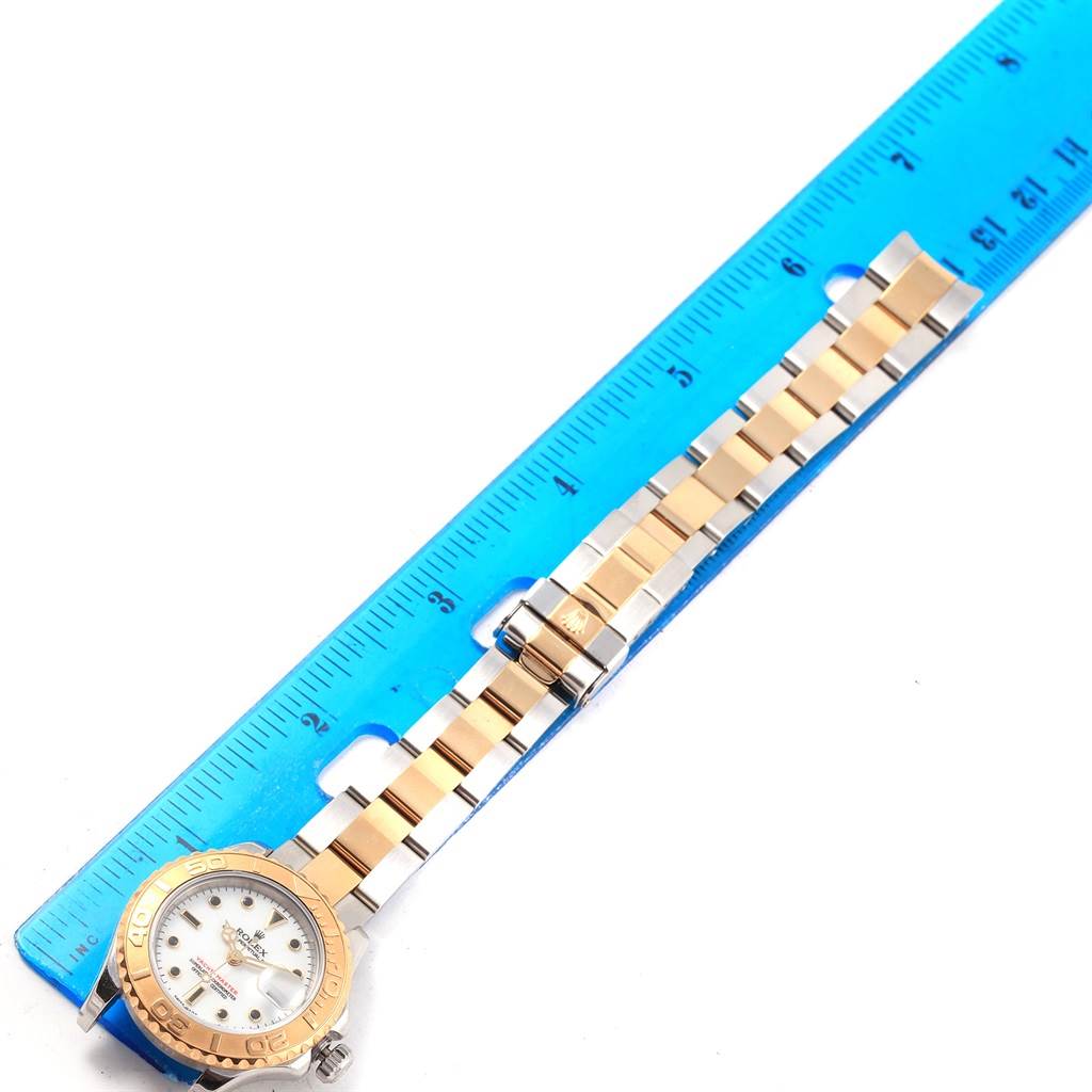 The Rolex Yacht-Master 169623 Women
s Steel and Gold (two tone) White Dial 169623 Women
s Steel and Gold (two tone) White Dial watch is shown with its case, bezel, and full bracelet laid next to a ruler for measurement.