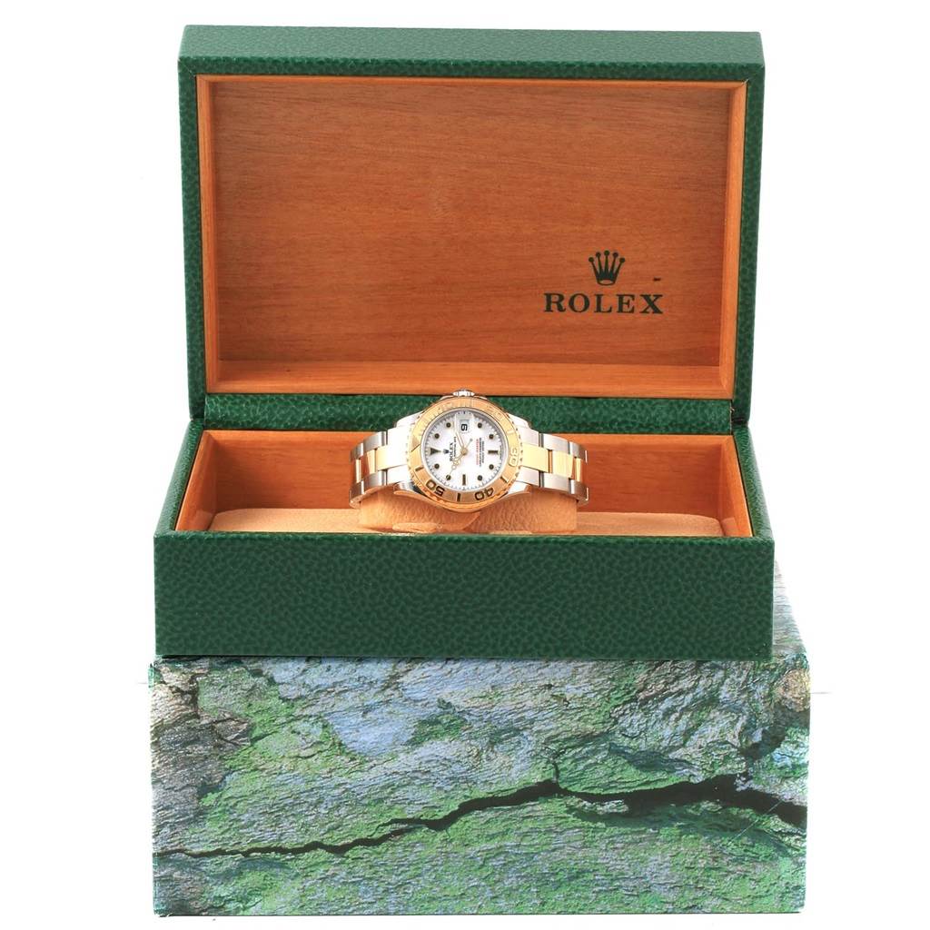 The Rolex Yacht-Master 169623 Women
s Steel and Gold (two tone) White Dial 169623 Women
s Steel and Gold (two tone) White Dial watch is shown from the front, resting inside an open green and wood-finished Rolex box.