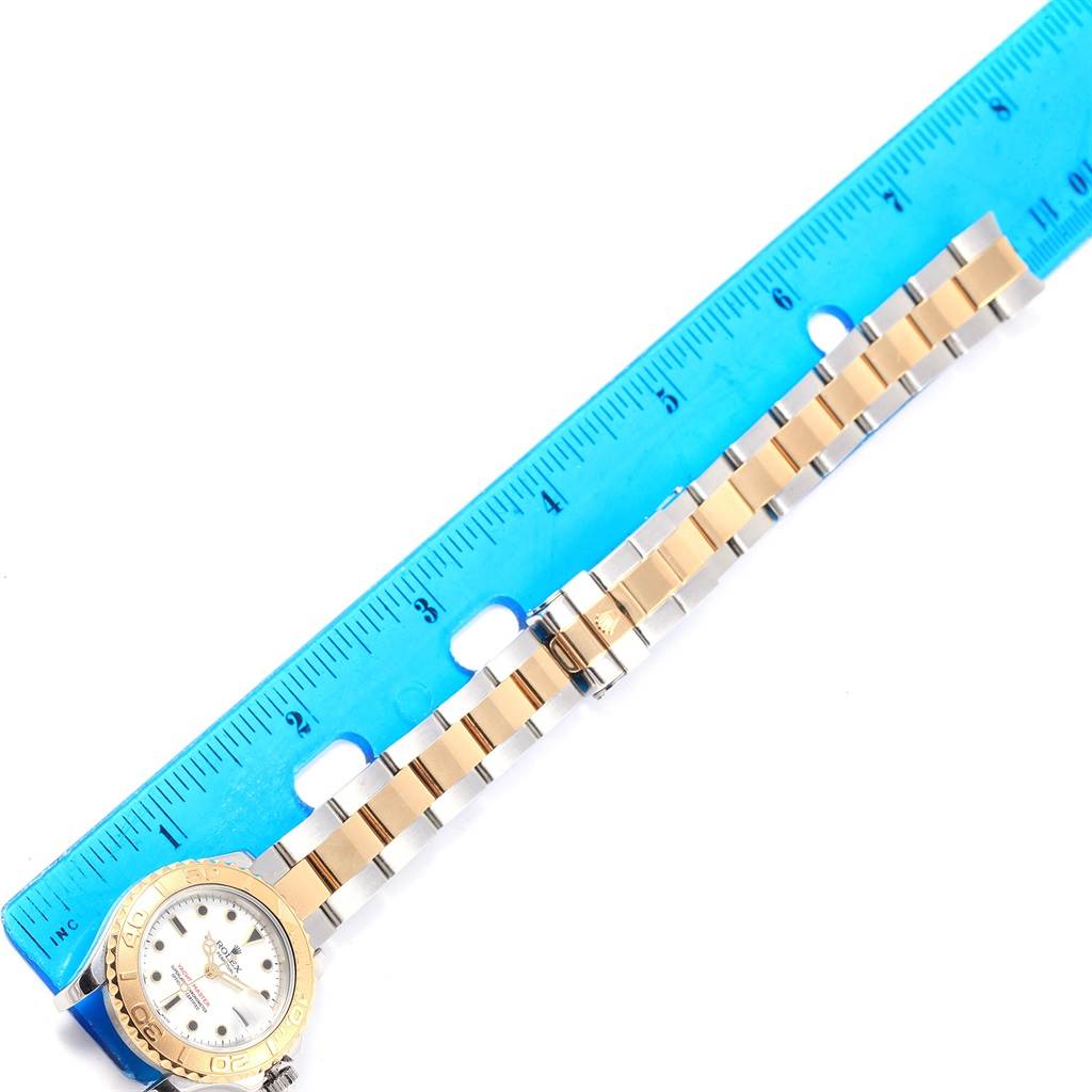 The image shows a Rolex Yacht-Master 169623 Women
s Steel and Gold (two tone) White Dial 169623 Women
s Steel and Gold (two tone) White Dial watch placed next to a blue ruler, highlighting the bracelet and clasp.