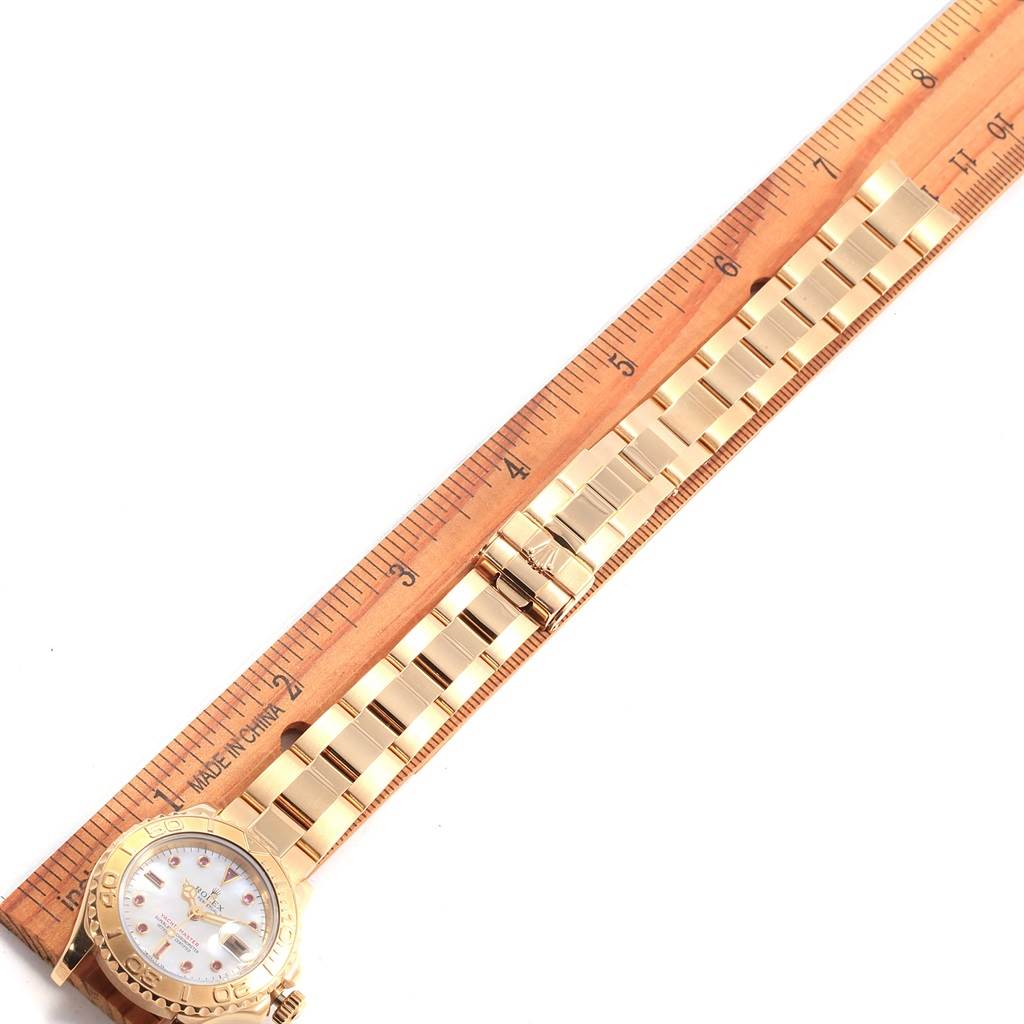 The image shows a Rolex Yacht-Master 69628 Women's Yellow Gold Mother of Pearl Dial 69628 Women's Yellow Gold Mother of Pearl Dial watch laid flat next to a ruler, showcasing its face and bracelet.