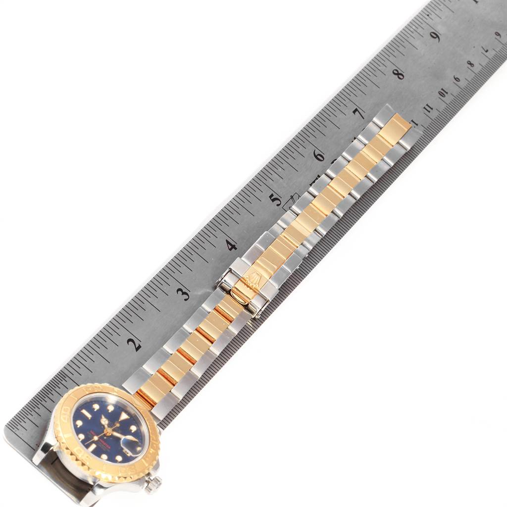 The image shows the Yacht-Master watch by Rolex laid flat next to a ruler, highlighting the entirety of the bracelet and part of the watch dial.