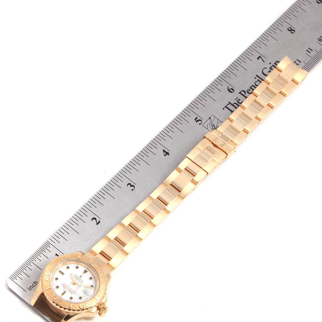 The image shows a Rolex Yacht-Master 169628 Women's Yellow Gold White Dial 169628 Women's Yellow Gold White Dial watch laid flat next to a ruler, displaying its face and band.
