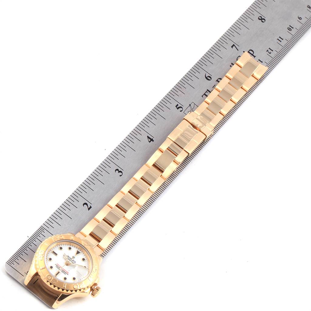 The image shows a top view of a Rolex Yacht-Master 169628 Women's Yellow Gold White Dial 169628 Women's Yellow Gold White Dial watch with its band laid alongside a ruler for measurement.