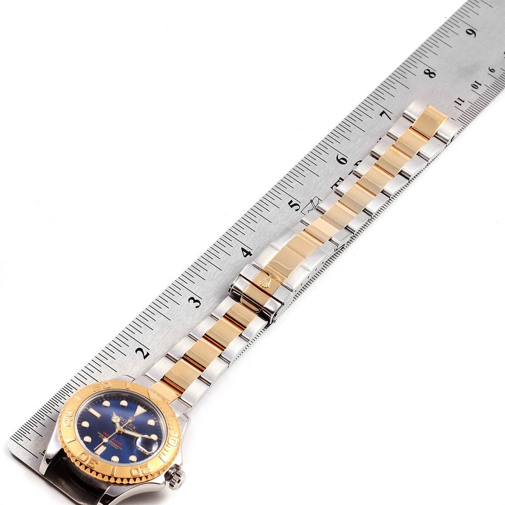 The Rolex Yacht-Master 168623 Men's Steel and Gold (two tone) Blue Dial 168623 Men's Steel and Gold (two tone) Blue Dial watch is shown from a top-down angle, highlighting the dial, bezel, and bracelet beside a ruler for scale.