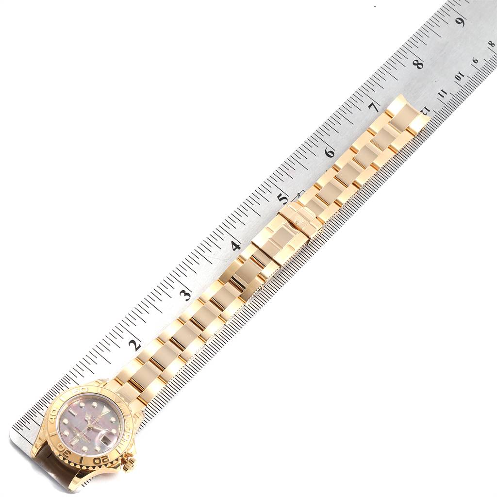 The image shows a Rolex Yacht-Master 169628 Women's Yellow Gold Mother of Pearl Dial 169628 Women's Yellow Gold Mother of Pearl Dial watch laid next to a ruler, highlighting the watch's bezel, dial, and bracelet.