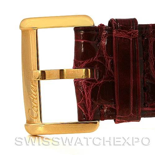The image shows a close-up of a Tank Divan model by Cartier, focusing on its gold buckle and red leather strap.