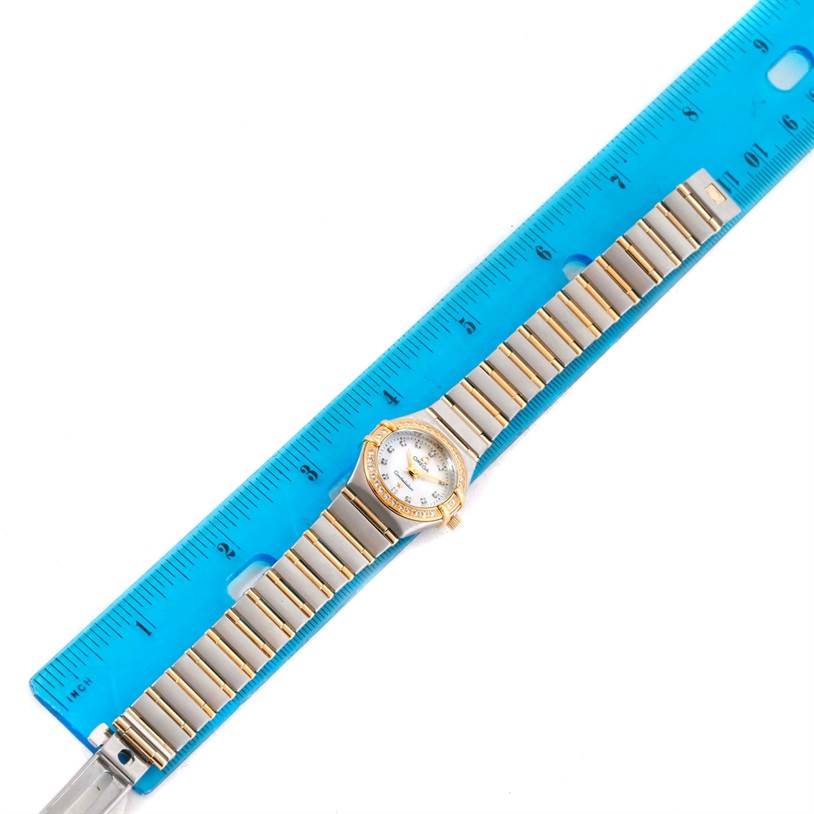 The image shows an Omega 1267.75.00 Women
s Steel and Gold (two tone) Mother of Pearl Dial 1267.75.00 Women
s Steel and Gold (two tone) Mother of Pearl Dial Constellation My Choice Mini Steel Gold Diamond Watch 1267.75.00 laid flat beside a blue ruler for scale.