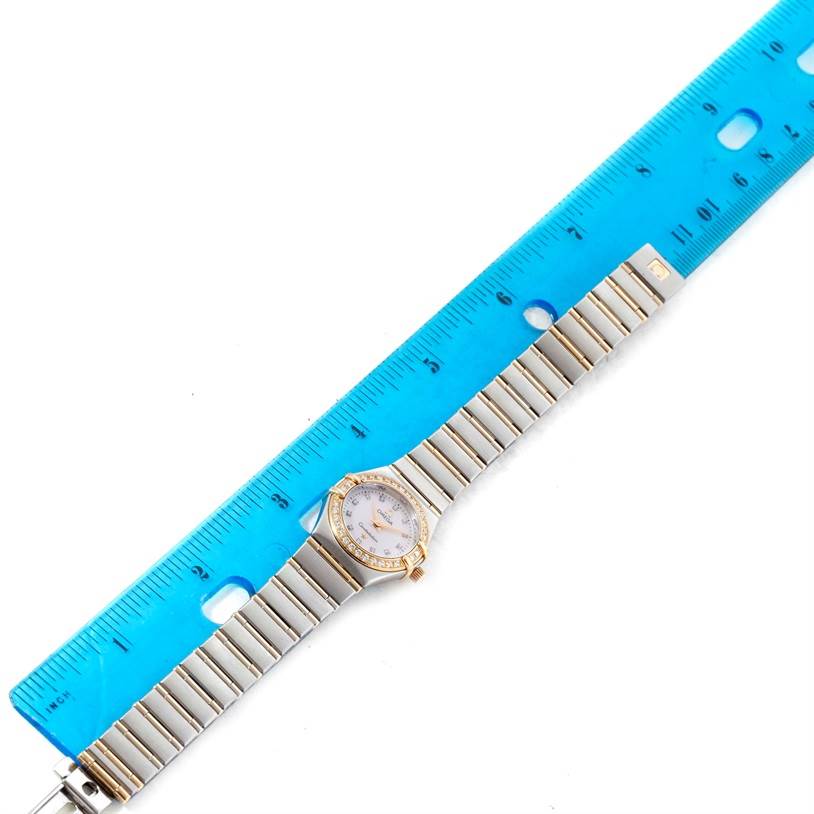The Omega 1267.75.00 Women
s Steel and Gold (two tone) Mother of Pearl Dial 1267.75.00 Women
s Steel and Gold (two tone) Mother of Pearl Dial Constellation My Choice Mini Diamond Watch 1267.75.00 is shown flat, next to a blue ruler for measurement.