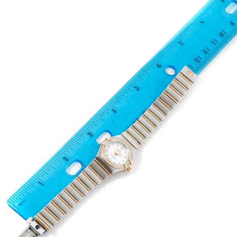 This is an overhead view of the Omega 1267.75.00 Women
s Steel and Gold (two tone) Mother of Pearl Dial 1267.75.00 Women
s Steel and Gold (two tone) Mother of Pearl Dial Constellation My Choice Mini Two Tone Diamond Watch 1267.75.00 placed next to a ruler.