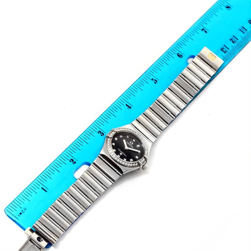 The image shows an Omega 1475.51.00 Women
s Stainless Steel Black Dial 1475.51.00 Women
s Stainless Steel Black Dial Constellation My Choice Ladies Diamond Watch 1475.51.00 laid flat next to a blue ruler for scale.