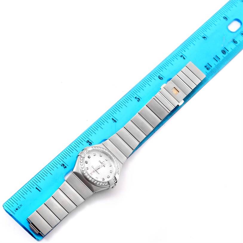 The image shows an Omega 123.15.27.60.52.001 Women
s Stainless Steel Silver Dial 123.15.27.60.52.001 Women
s Stainless Steel Silver Dial Constellation 27mm Diamond Ladies Watch model 123.15.27.60.52.001 placed next to a blue ruler for scale.