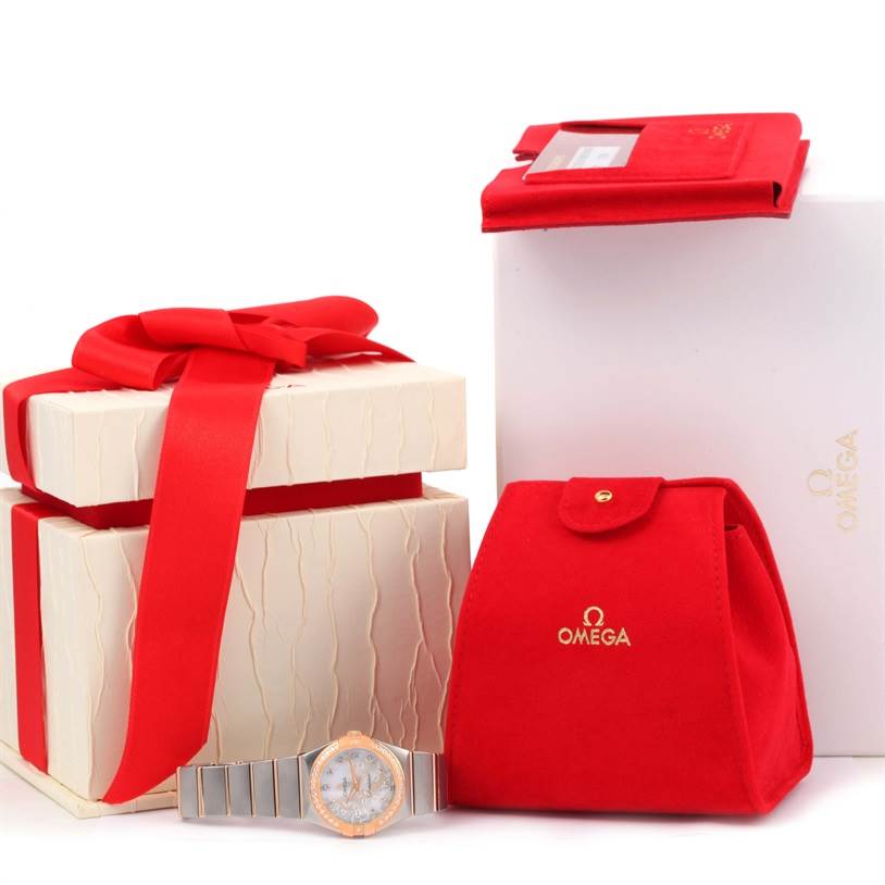 The image shows an Omega 123.25.27.60.55.009 Women
s Steel and Gold (two tone) Mother of Pearl Dial 123.25.27.60.55.009 Women
s Steel and Gold (two tone) Mother of Pearl Dial Constellation Diamond Steel Rose Gold Watch 123.25.27.60.55.009 and its packaging accessories from a front angle.