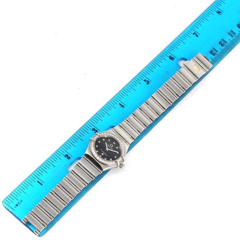 The image shows an Omega 1465.51.00 Women
s Stainless Steel Black Dial 1465.51.00 Women
s Stainless Steel Black Dial Constellation My Choice Mini Ladies Diamond Watch 1465.51.00 placed on top of a blue ruler.