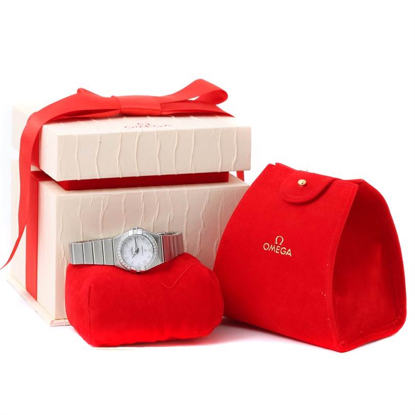 The image shows an Omega 123.15.24.60.55.004 Women's Stainless Steel Mother of Pearl Dial 123.15.24.60.55.004 Women's Stainless Steel Mother of Pearl Dial Constellation Steel MOP Diamond Watch 123.15.24.60.55.004 laid out with packaging, including a red box and pouch.