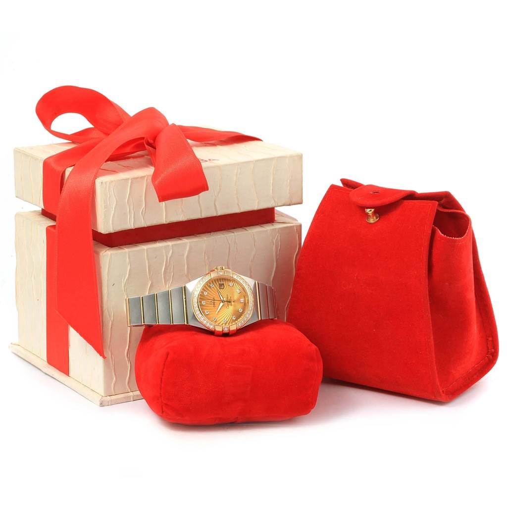 The Omega 123.25.31.20.58.001 Women
s Steel and Gold (two tone) Champagne Dial 123.25.31.20.58.001 Women
s Steel and Gold (two tone) Champagne Dial Constellation 31 Co-Axial Diamond Ladies Watch is shown front-facing, displayed on a red cushion, next to a gift box and a red pouch.