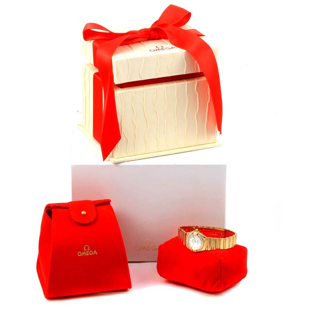 The image shows an Omega 1164.75.00 Women's Yellow Gold Mother of Pearl Dial 1164.75.00 Women's Yellow Gold Mother of Pearl Dial Constellation My Choice model 1164.75.00 watch with its packaging, including a gift box, a red pouch, and a watch pillow.
