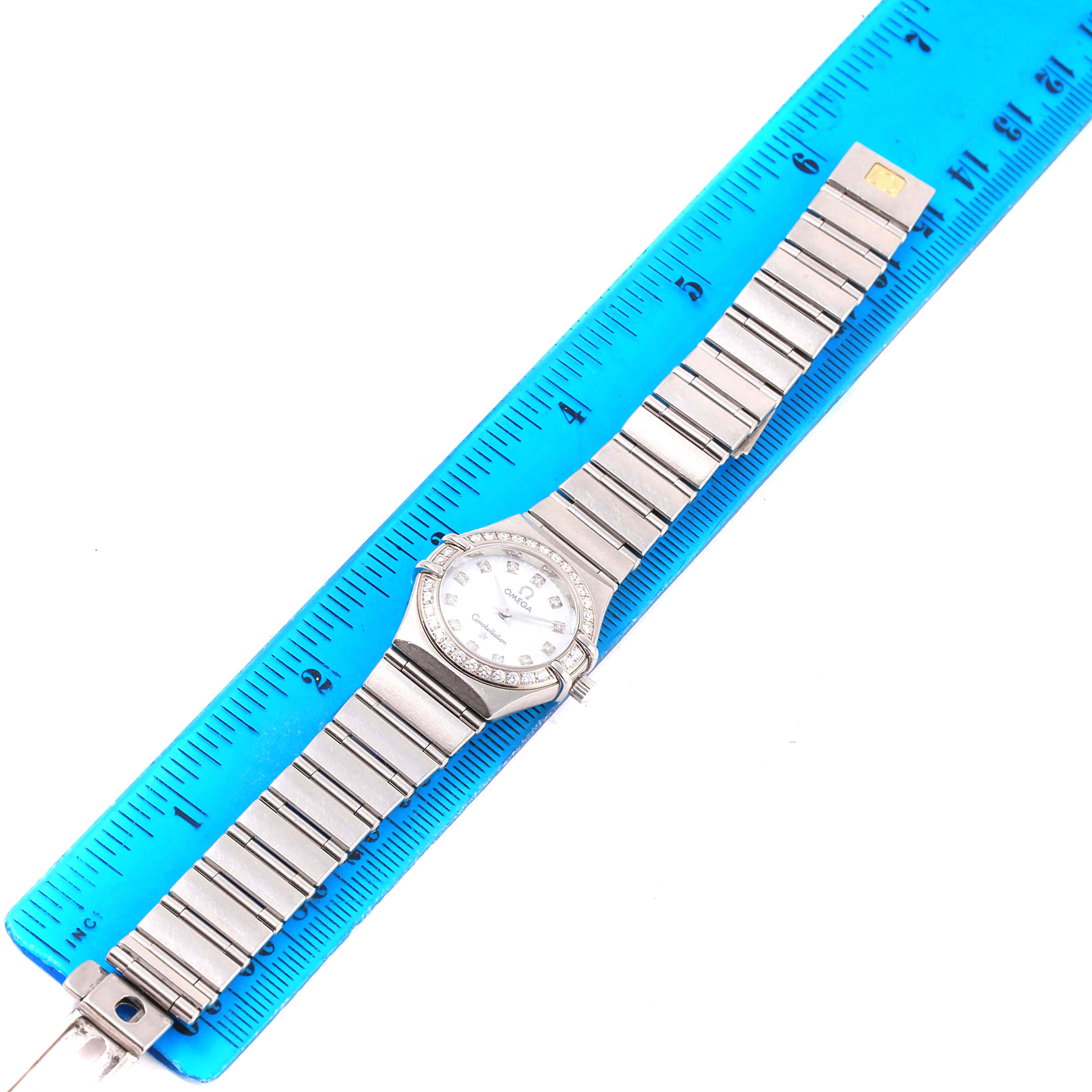 The Omega 1460.75.00 Women's Stainless Steel Mother of Pearl Dial 1460.75.00 Women's Stainless Steel Mother of Pearl Dial Constellation 95 Mini Diamond Ladies Watch 1460.75.00 is shown flat with its full bracelet length next to a blue ruler.