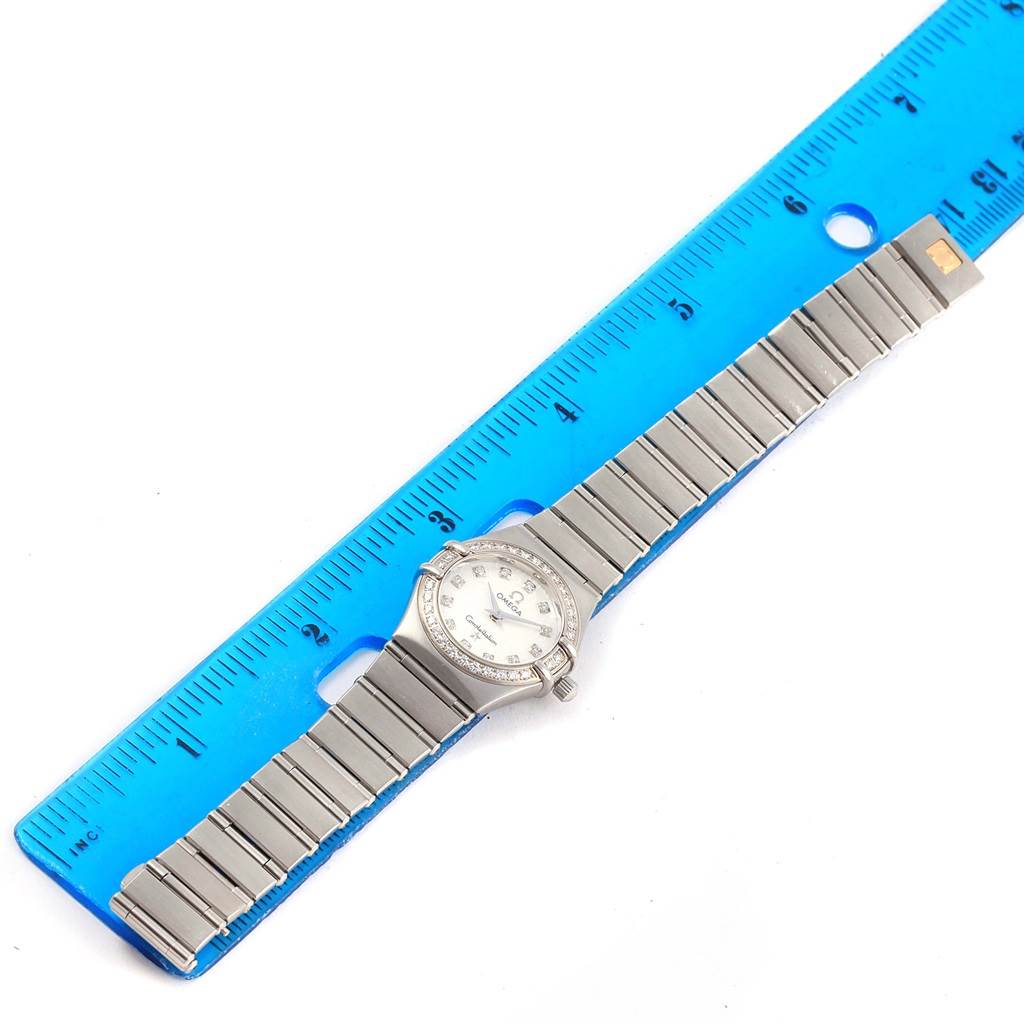 The image shows an Omega 1460.75.00 Women
s Stainless Steel Mother of Pearl Dial 1460.75.00 Women
s Stainless Steel Mother of Pearl Dial Constellation 95 Mini MOP Diamonds Ladies Watch 1460.75.00 laid flat next to a blue ruler.