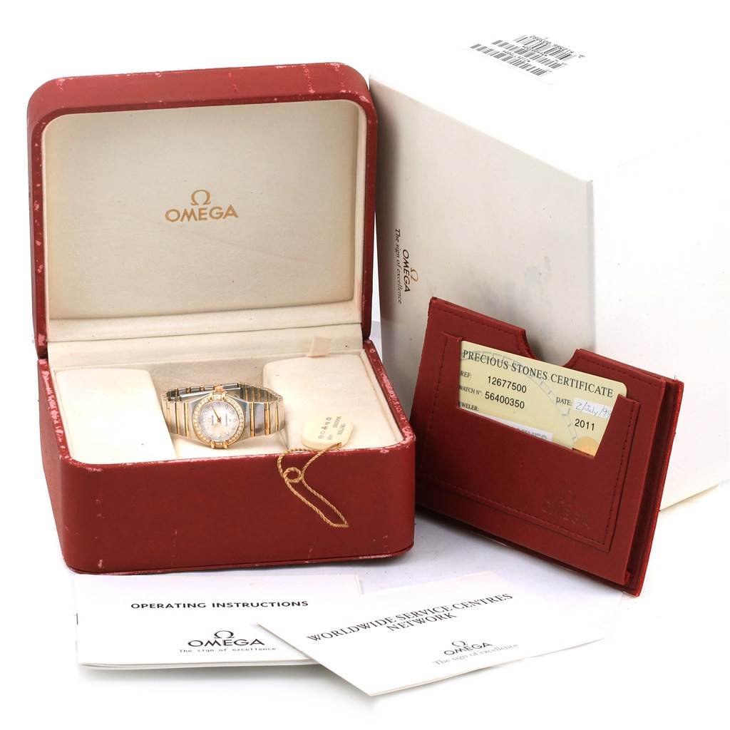 The image shows an Omega 1267.75.00 Women
s Steel and Gold (two tone) Mother of Pearl Dial 1267.75.00 Women
s Steel and Gold (two tone) Mother of Pearl Dial Constellation Mini MOP Diamond Ladies Watch 1267.75.00 in its open box, alongside certification and paperwork.
