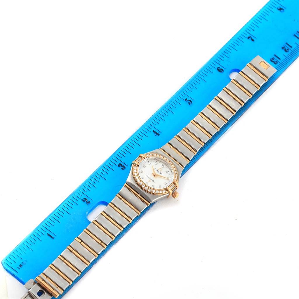The image shows an Omega 1267.75.00 Women
s Steel and Gold (two tone) Mother of Pearl Dial 1267.75.00 Women
s Steel and Gold (two tone) Mother of Pearl Dial Constellation Mini MOP Diamond Ladies Watch 1267.75.00 fully extended and measured with a blue ruler.