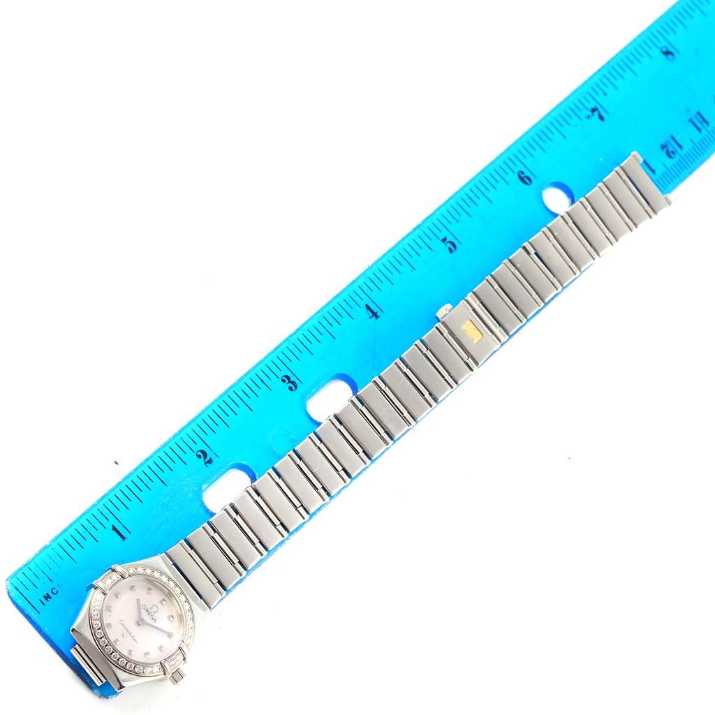 The image shows an Omega 1465.71.00 Women
s Stainless Steel Mother of Pearl Dial 1465.71.00 Women
s Stainless Steel Mother of Pearl Dial Constellation My Choice Mini Diamond Steel Watch 1465.71.00 stretched out next to a blue ruler for measurement.