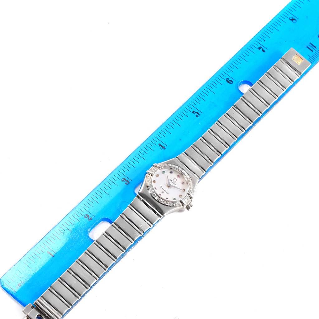 The image shows the Omega 1460.79.00 Women's Stainless Steel Mother of Pearl Dial 1460.79.00 Women's Stainless Steel Mother of Pearl Dial Constellation Iris Rainbow Multi Stone Watch 1460.79.00 lying flat with a blue ruler for scale.
