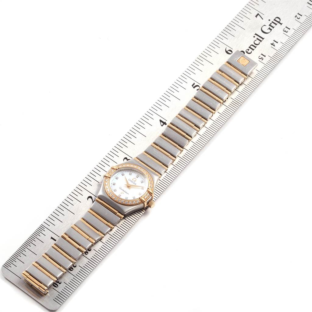 The Omega 1267.75.00 Women's Steel and Gold (two tone) Mother of Pearl Dial 1267.75.00 Women's Steel and Gold (two tone) Mother of Pearl Dial Constellation Mini Mother of Pearl Diamond Watch 1267.75.00 is shown from a top-down angle with its band aligned alongside a ruler.