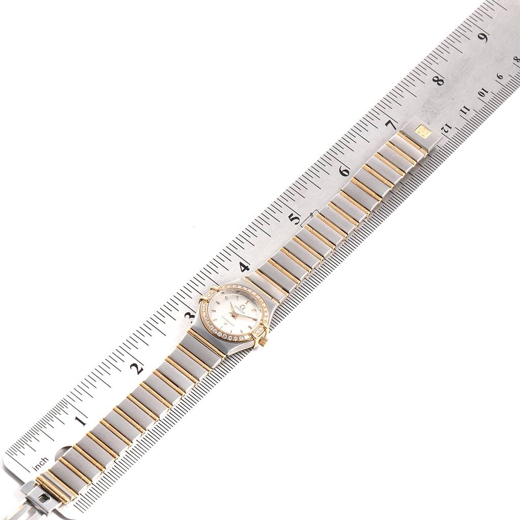 The Omega 1267.30.00 Women's Steel and Gold (two tone) Silver Dial 1267.30.00 Women's Steel and Gold (two tone) Silver Dial Constellation 95 model 1267.30.00 watch is shown from a top-down angle on a ruler, displaying the entire watch and bracelet.