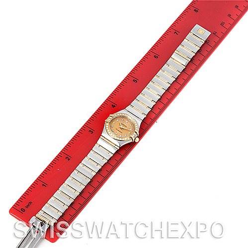 The image shows an Omega 1267.15.00 Women
s Steel and Gold (two tone) Champagne Dial 1267.15.00 Women
s Steel and Gold (two tone) Champagne Dial Constellation Mini Steel 18K Yellow Gold Diamond 1267.15.00 Watch laying flat next to a red ruler for scale.
