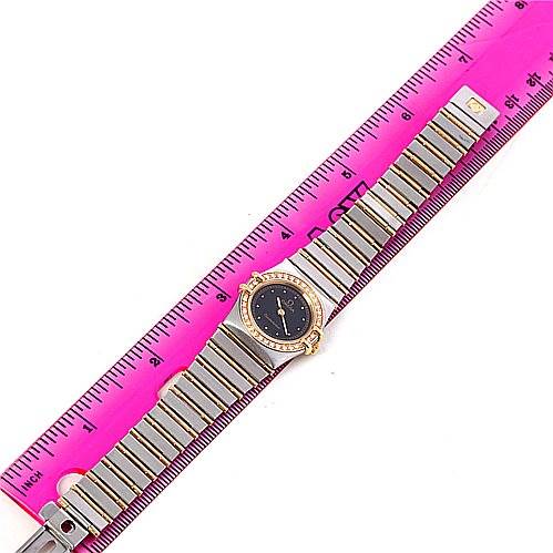 The Omega 1267.10.00 Women
s Steel and Gold (two tone) Black Dial 1267.10.00 Women
s Steel and Gold (two tone) Black Dial Constellation Diamond Mini 1267.10.00 watch is shown laid flat, with the entire bracelet and face visible, alongside a pink ruler for scale.
