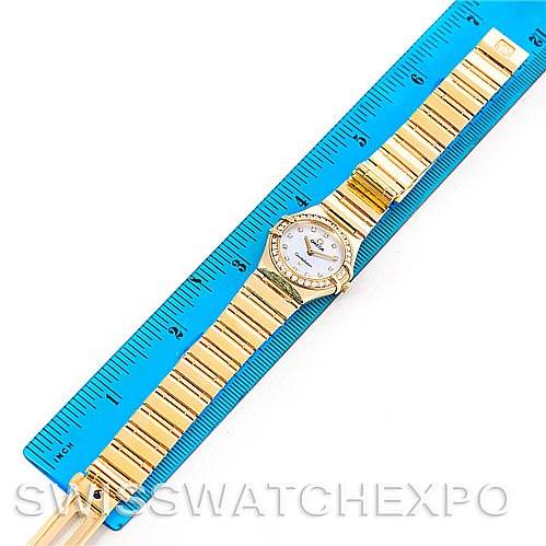 The image shows the top view of the Omega 1164.75.00 Women's Yellow Gold Mother of Pearl Dial 1164.75.00 Women's Yellow Gold Mother of Pearl Dial Constellation 18K Yellow Gold Diamond Mini 1164.75.00 watch next to a blue ruler for sizing.