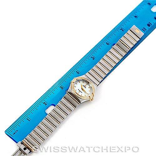 The image shows an overhead view of the Omega 1277.70.00 Women
s Steel and Gold (two tone) Mother of Pearl Dial 1277.70.00 Women
s Steel and Gold (two tone) Mother of Pearl Dial Constellation My Choice Steel Gold Diamond Watch 1277.70.00 next to a blue ruler.