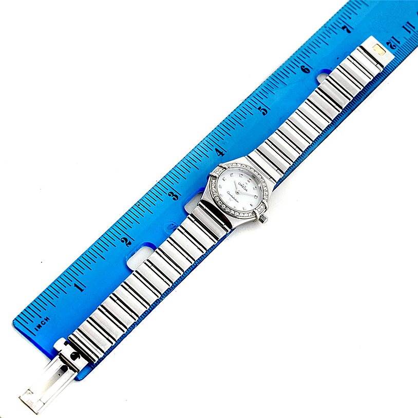 The image shows the Omega 1465.71.00 Women
s Stainless Steel Mother of Pearl Dial 1465.71.00 Women
s Stainless Steel Mother of Pearl Dial Constellation My Choice Ladies Diamond Mini Watch 1465.71.00 laying flat next to a ruler for scale.