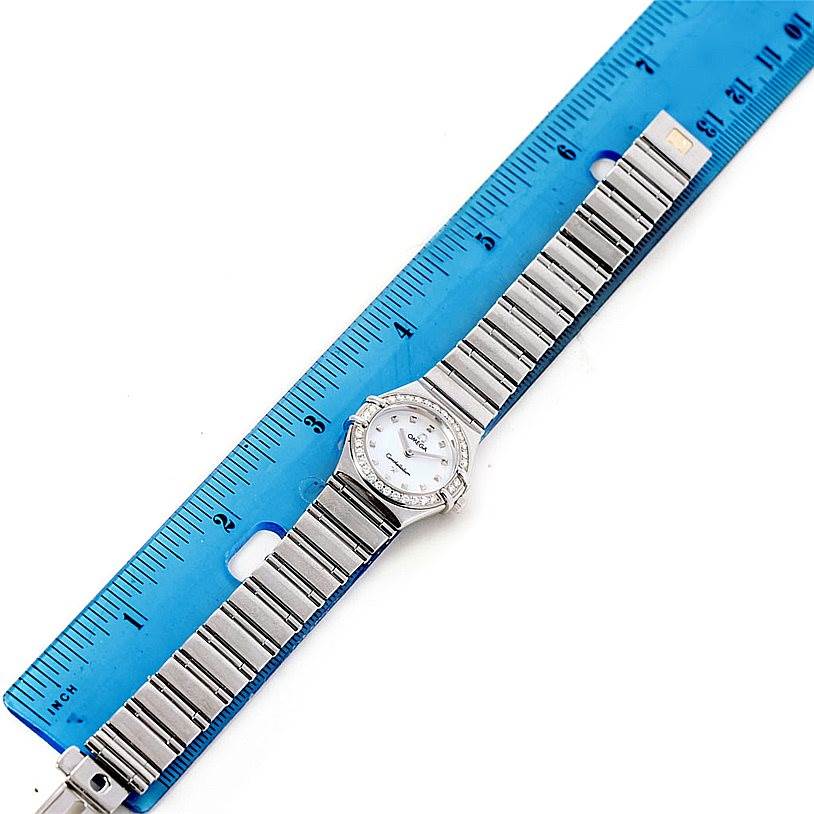 The image shows a top view of the Omega 1465.71.00 Women
s Stainless Steel Mother of Pearl Dial 1465.71.00 Women
s Stainless Steel Mother of Pearl Dial Constellation My Choice Ladies Mini Diamond Watch 1465.71.00 next to a blue ruler.