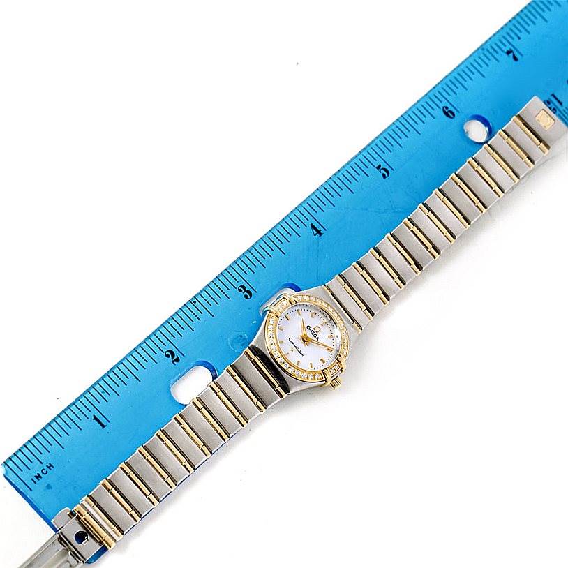 The Omega 1267.70.00 Women
s Steel and Gold (two tone) Mother of Pearl Dial 1267.70.00 Women
s Steel and Gold (two tone) Mother of Pearl Dial Constellation Ladies Diamond Mini Watch 1267.70.00 is shown laid flat beside a blue ruler.