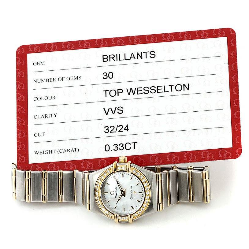 The image shows an Omega 1267.70.00 Women
s Steel and Gold (two tone) Mother of Pearl Dial 1267.70.00 Women
s Steel and Gold (two tone) Mother of Pearl Dial Constellation Ladies Diamond Mini Watch model 1267.70.00 laid flat beside a gem certification card.