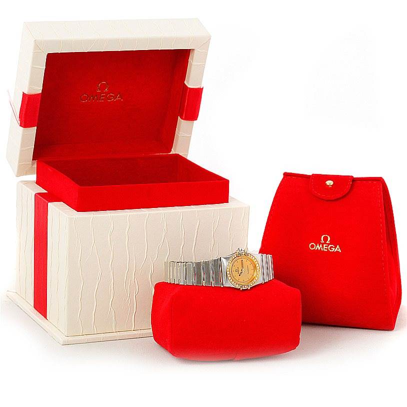 The image displays an Omega Women
s Steel and Gold (two tone) Champagne Dial Women
s Steel and Gold (two tone) Champagne Dial Constellation Mini Steel 18K Yellow Gold Diamond Watch with its case and pouch at an oblique angle.
